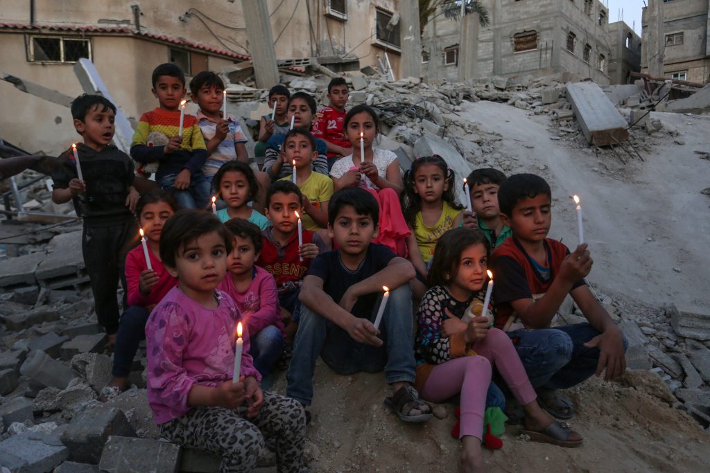 Palestinian children holding candles on top of the rubble of a house destroyed in Israeli air strike