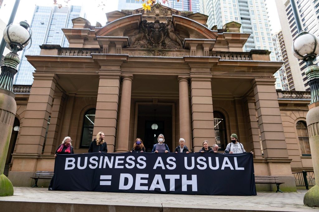 Blockade Australia protesters at Sydney Townhall during the climate action week 27 June - 2 July 2022 holding a banner with the message Business As Usual equals Death