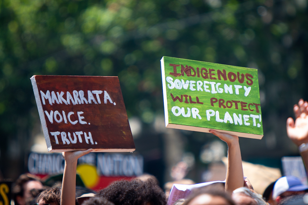 Protest signs at Invasion Day march in Melbourne in 2020 read 'Makarrata. Voice. Truth.' and 'Indigenous Sovereignty Will Protect Our Planet'